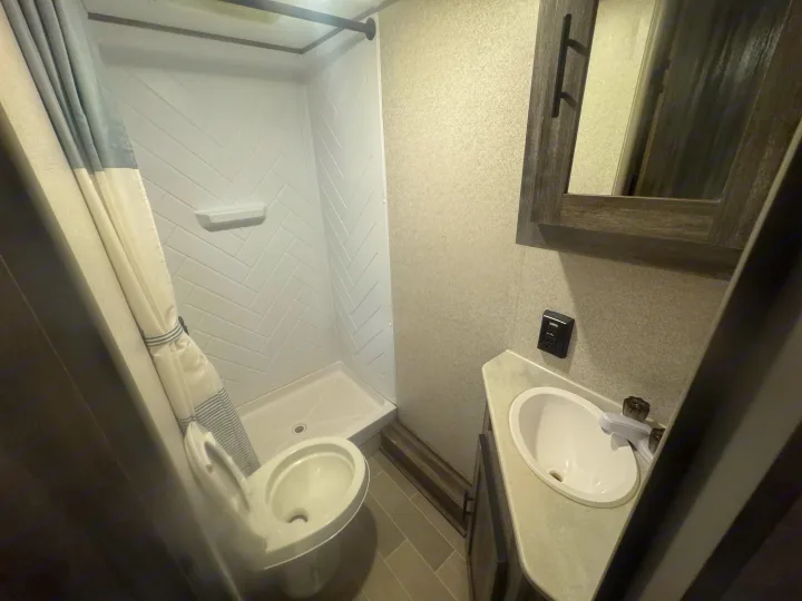 Compact RV rental bathroom featuring a white herringbone shower, toilet, and sink, perfect for on-the-go trips.. Forest River Salem 2021