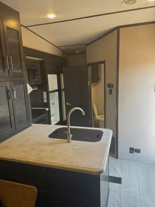 This RV rental features a modern kitchen with a sink, microwave, fridge, stove, and dark cabinetry. A bathroom with toilet is visible.. Forest River Nitro Xlr 2017