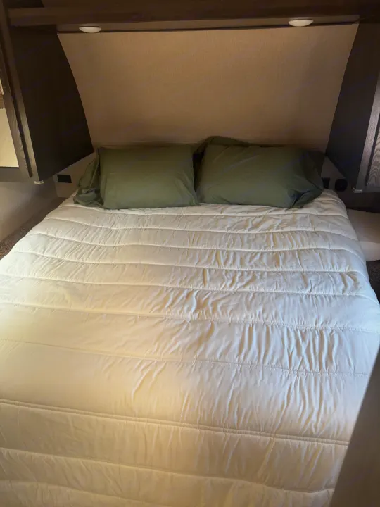 Inside an RV rental: A neat bed with a white quilted comforter and olive pillows, showcasing the cozy sleeping area.. Forest River Nitro Xlr 2017