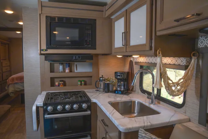 Explore this inviting rv rental kitchen, boasting a microwave, stove, sink, and coffee maker, extending to a cozy bedroom.. Thor Motor Coach Coleman 2023