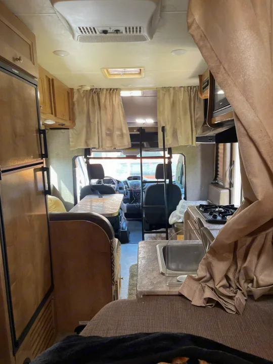 Well-equipped rv rental interior with kitchen (sink, stove), dining booth, and driver's cockpit view.. Coachmen Leprechaun 2021