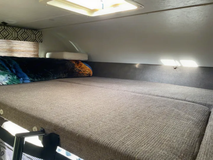Cozy rv rental overhead sleeping area with textured gray bed cushions, dark headboard, and bright skylight.. Coachmen Leprechaun 2021