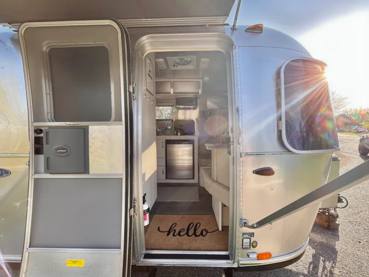 Explore a sleek Airstream travel trailer RV rental, bathed in sunlight. The open door invites you into its compact, modern interior.. Airstream Sport 2018