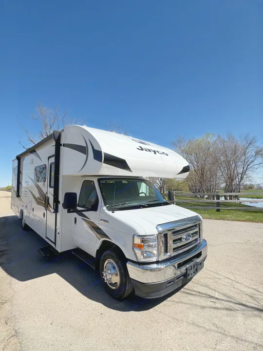 White Jayco Class C RV rental parked on a paved road, bathed in sunlight under a clear blue sky.. Jayco Redhawk 2024