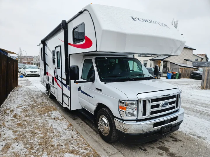 A large white Forester RV rental with red and blue accents is parked on a snow-dusted street in a residential neighborhood.. Forester 2651 CDW 2022