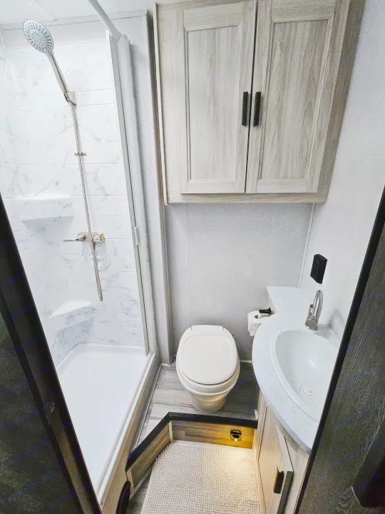 Inside an RV rental: a modern, compact bathroom with a shower, toilet, sink vanity, and light-wood cabinets.. Forester 2651 CDW 2022