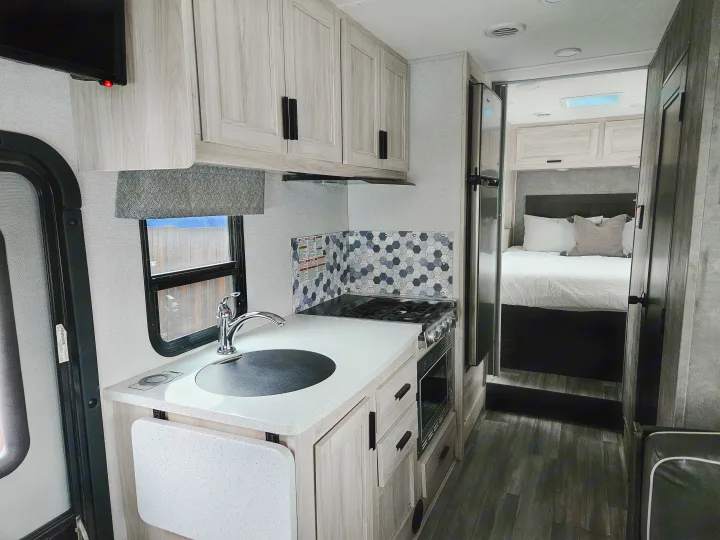 Modern RV rental interior: well-equipped kitchen with sink, stove, and light cabinets, leading to a cozy bedroom.. Forester 2651 CDW 2022