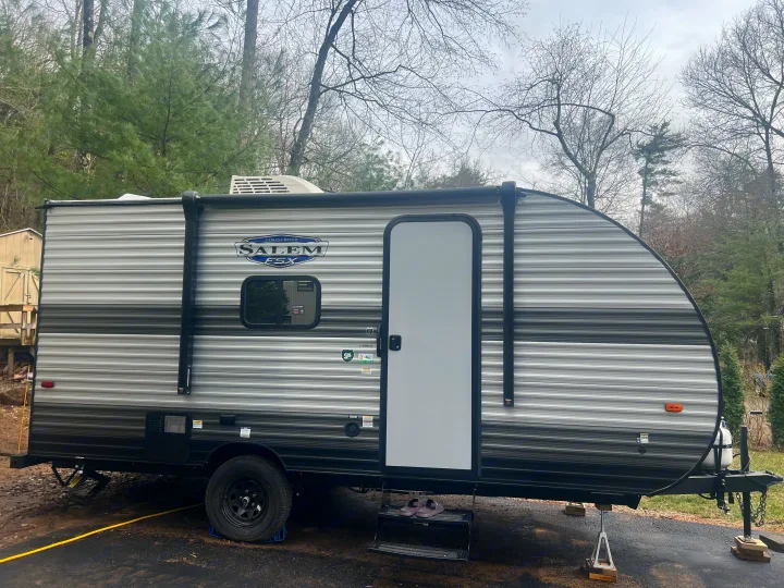 A grey striped Forest River Salem FSX travel trailer (RV) is parked and stabilized on a paved surface, ready for an rv rental trip.. Forest River Salem 2024