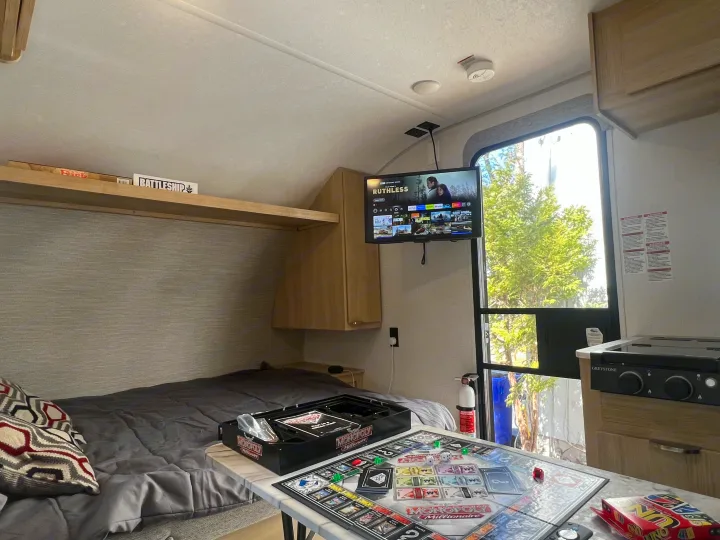 Cozy RV rental interior with board games (Monopoly, Battleship), TV, and compact kitchen.. Forest River Salem 2024