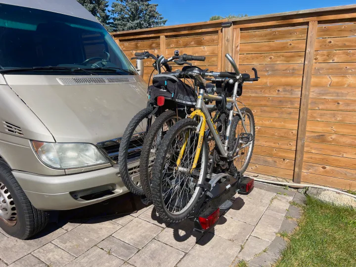 RV rental van with two bicycles on a rear rack, parked by a wooden fence on a sunny day.. Mercedes-Benz Sprinter 2006