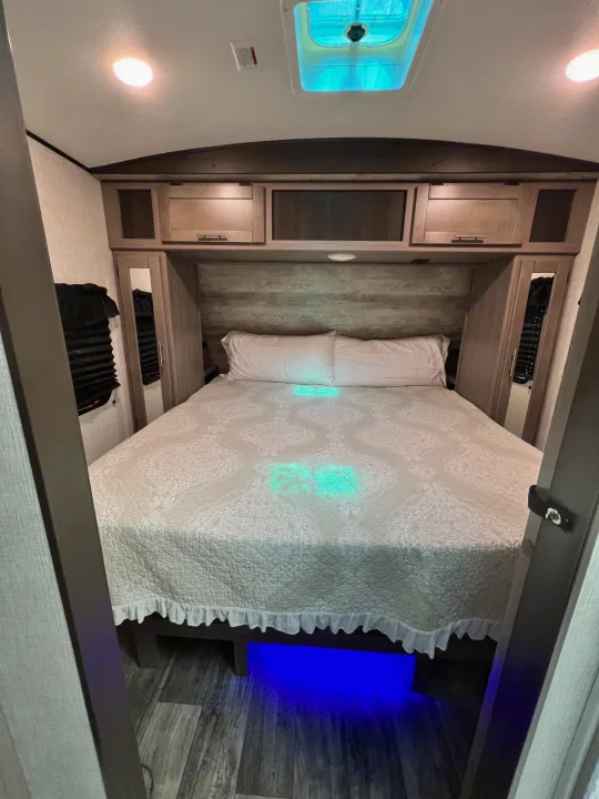 Cozy RV rental bedroom with modern overhead cabinets, bright lighting, and ambient blue under-bed glow for a comfortable stay.. Crossroads RV Sunset Trail Super Lite 2021