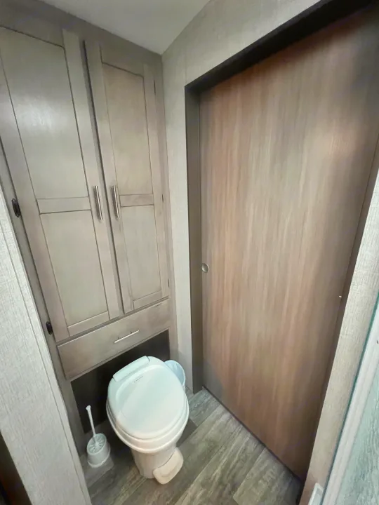 RV rental's compact bathroom with a small toilet, built-in light grey cabinets, and wood-look door and floor.. Crossroads RV Sunset Trail Super Lite 2021