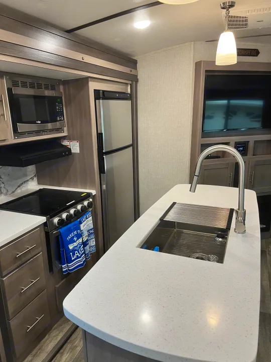Spacious rv rental interior: modern kitchen with island sink, microwave, fridge, stove, and living area with TV. Great for trips!. Crossroads RV Sunset Trail Super Lite 2021