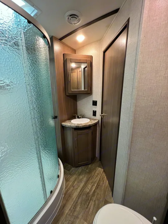 Efficient RV rental bathroom with curved glass shower, corner sink vanity, medicine cabinet, and toilet visible.. Crossroads RV Sunset Trail Super Lite 2021