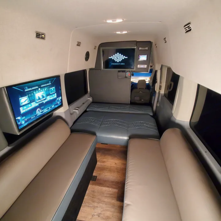 Spacious RV rental interior with convertible seating, two TVs, and wood flooring for comfort and entertainment.. Ford Custom Transit 2017