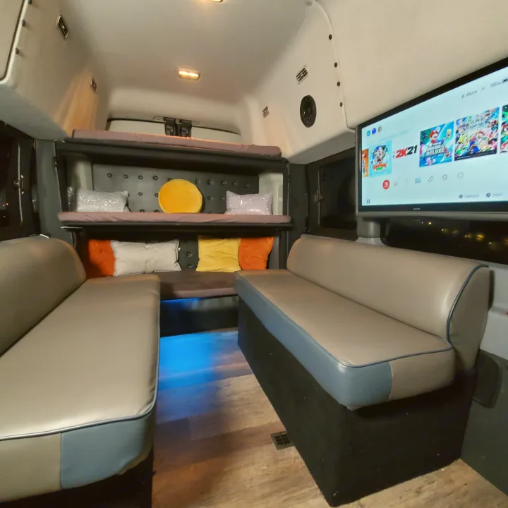 Inside a unique RV rental: two lounge sofas, bunk beds, a large TV for gaming, and cool blue ambient lighting.. Ford Custom Transit 2017