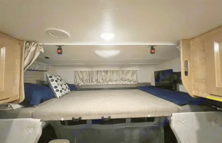 Cozy sleeping area in an RV rental, featuring a large bed, overhead lights, and storage cabinets for comfort.. Coachmen Leprechaun 260RS 2020