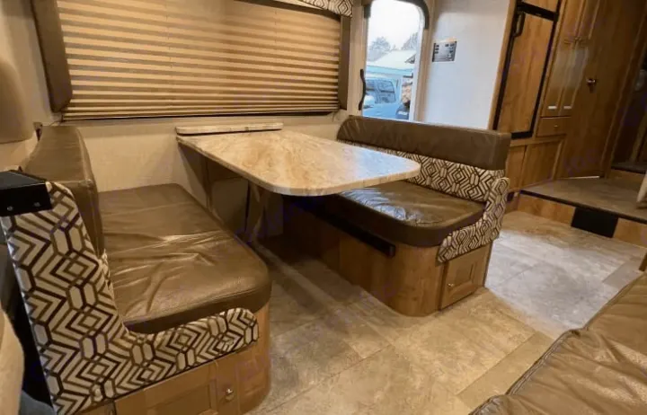 Spacious RV rental dinette with comfortable brown benches and a light-colored table, perfect for meals and relaxation.. Coachmen Leprechaun 260RS 2020