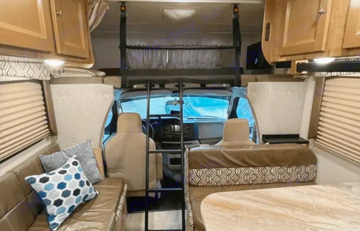 View inside a modern RV rental: living area, dining booth, and over-cab bunk bed with ladder.. Coachmen Leprechaun 260RS 2020