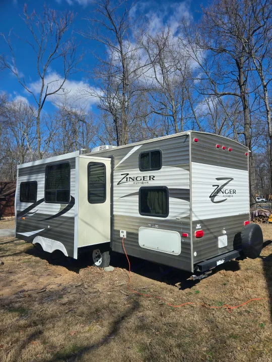 Experience outdoor living! This Zinger travel trailer, an ideal rv rental, is parked with its slide-out extended under a clear sky.. Crossroads RV Zinger 2014