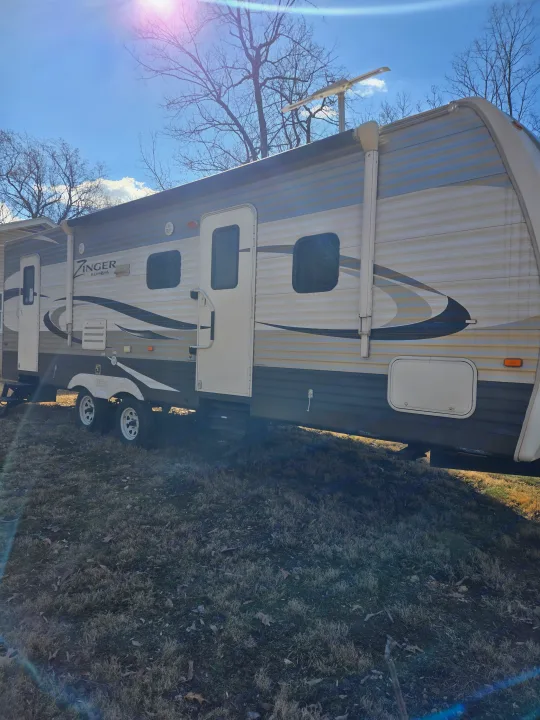 Experience adventure with this Zinger travel trailer RV rental. A large, two-door camper parked on grassy terrain under sunny skies.. Crossroads RV Zinger 2014