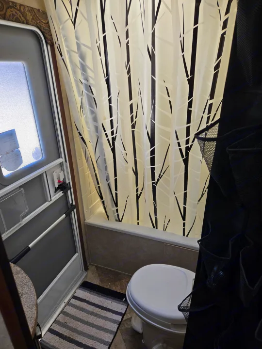 Inside an RV rental: a compact bathroom featuring a stylish birch tree shower curtain, toilet, and screen door.. Crossroads RV Zinger 2014