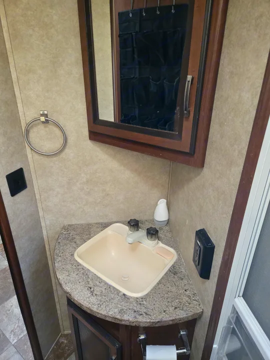 Compact RV rental bathroom with a corner sink, mirrored cabinet, towel ring, and toilet paper holder.. Crossroads RV Zinger 2014