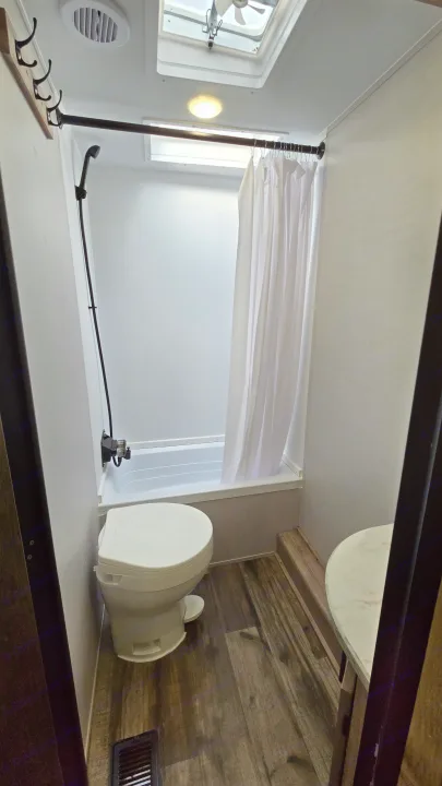 Clean RV rental bathroom featuring a compact toilet, shower/tub combo, and a white shower curtain.. Gulf Stream Trailmaster 2024
