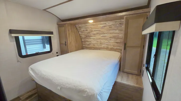 Spacious RV rental bedroom with a comfy bed, modern headboard, built-in storage closets, and windows for natural light.. Gulf Stream Trailmaster 2024