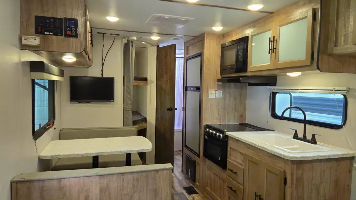 RV rental interior features a modern kitchen, cozy dinette, and visible bunk beds, ideal for travel.. Gulf Stream Trailmaster 2024
