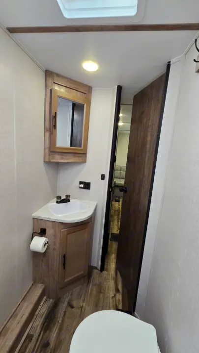 Inside an RV rental: a compact bathroom featuring a corner sink, mirrored cabinet, light, and a glimpse of the toilet.. Gulf Stream Trailmaster 2024
