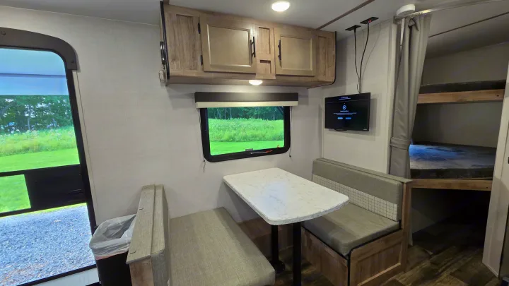 RV rental interior: A cozy dinette, overhead cabinets, wall-mounted TV, and bunk beds for comfortable travel.. Gulf Stream Trailmaster 2024