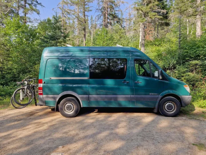 Green Mercedes Sprinter RV rental van with bikes parked on a forest dirt road, ready for adventure.. Dodge Sprinter Van 2008