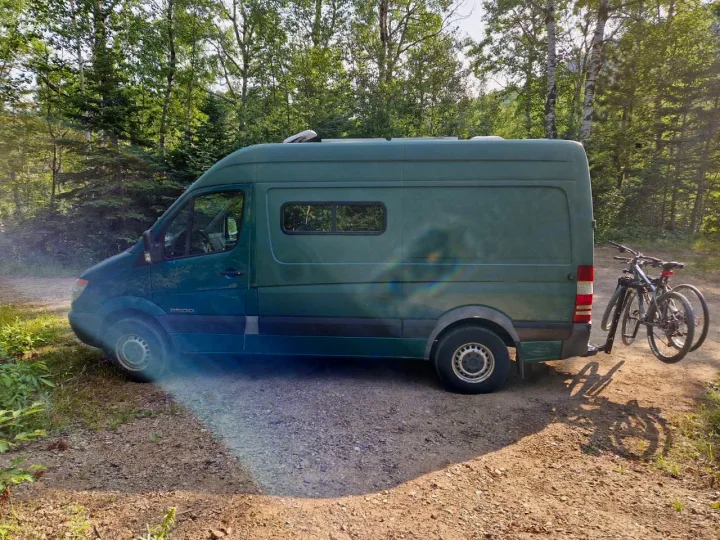 Green Sprinter camper van with bikes parked on a dirt road, perfect for an RV rental adventure in the forest.. Dodge Sprinter Van 2008