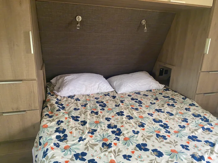 Cozy RV rental bedroom with floral bedding, built-in storage, and reading lights, showing a compact interior.. Grand Design Imagine 2021