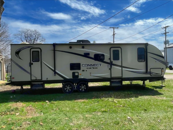 This beige Connect travel trailer RV rental, with dark graphics and two doors, sits on grass, ready for your outdoor adventure.. KZ Connect 2018