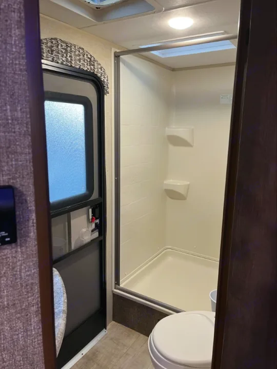 Compact RV rental bathroom featuring a stand-up shower, toilet, and a main entry door with a window.. KZ Connect 2018