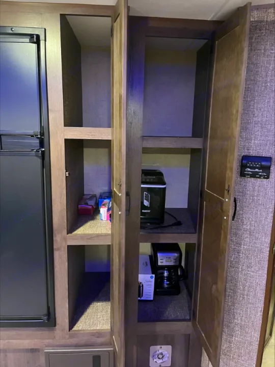 RV rental pantry showing a fridge, coffee maker, Igloo cooler, and various items on shelves.. KZ Connect 2018