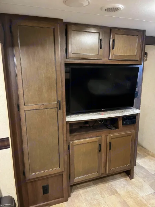 RV rental interior featuring a wooden entertainment center with TV, upper and lower cabinets, and a tall storage unit.. KZ Connect 2018