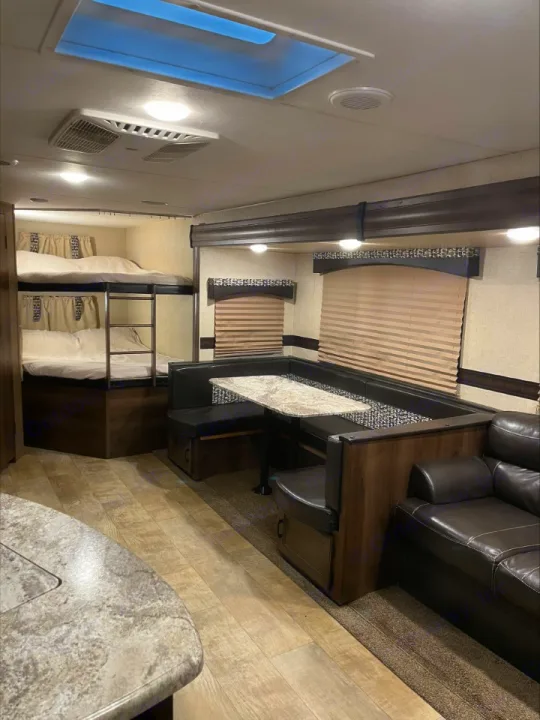 Spacious RV rental interior with bunk beds, U-shaped dinette, sofa, and kitchen counter. Well-lit and comfortable.. KZ Connect 2018