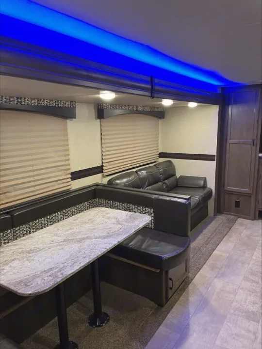 Modern RV rental living space with a U-shaped dining booth, comfy sofa, and ambient blue ceiling lights.. KZ Connect 2018