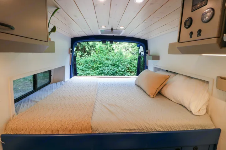 Cozy RV rental bedroom with a comfortable bed and stunning forest view from the rear doors.. Ford Transit 2016