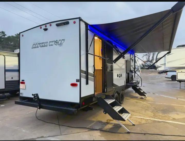 Modern white travel trailer RV rental, featuring an illuminated awning and deployed steps, ready for your trip.. Forest River Cherokee Alpha Wolf 2024