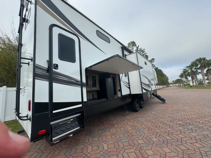 Spacious RV rental with open outdoor kitchen & steps. Perfect for camping, parked on a paved site surrounded by trees.. Forest River Sabre 2021