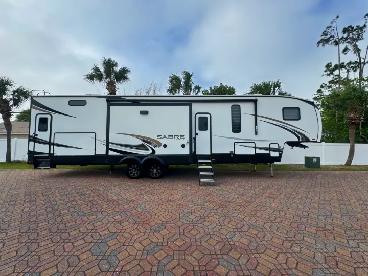 Experience travel with this Sabre Cobalt fifth wheel RV rental, set on a unique paver lot surrounded by palm trees.. Forest River Sabre 2021