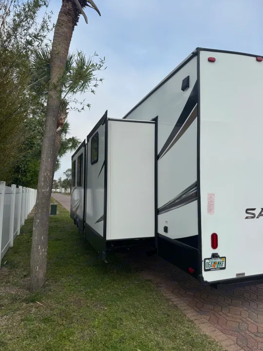 Spacious RV rental with slide-out extended, parked on pavers beside a palm tree at a Florida campground.. Forest River Sabre 2021