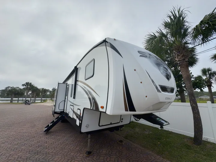 Spacious fifth-wheel RV rental parked on brick pavers, ready for your next travel adventure near a tranquil waterfront with palm trees.. Forest River Sabre 2021