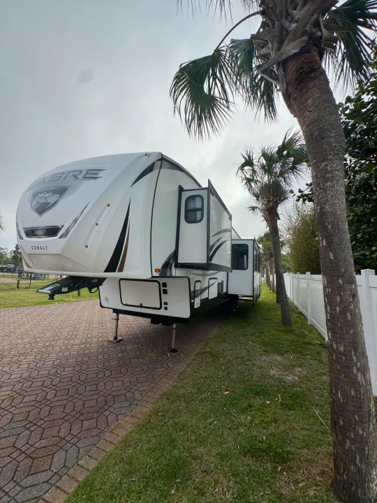 This large white Sabre Cobalt RV rental is set up on a paved site with extended slide-outs, surrounded by palm trees.. Forest River Sabre 2021