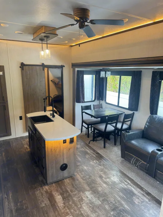 Spacious and modern RV rental interior featuring a full kitchen island, dining area, comfy recliners, and a bunk room.. Forest River Sabre 2021
