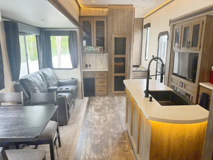 Modern RV rental interior with wood-look floors, a cozy living area, kitchen island, and dining space.. Forest River Sabre 2021